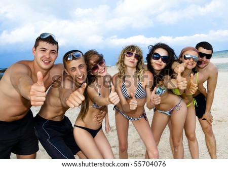 Joyful team of friends having fun at the beach and showing okay sign