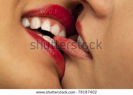 Closeup of pair women mouths kissing. One biting lip another