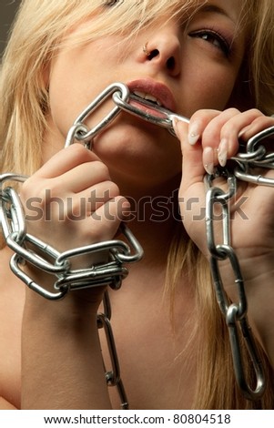 young caucasian woman biting a chrome chain over a dark background.
