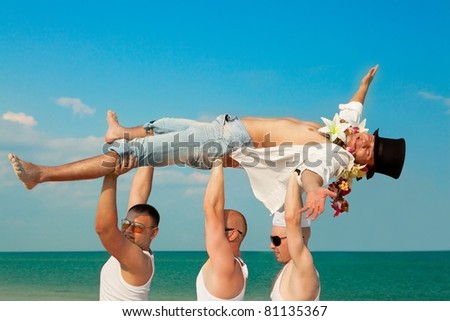 A happy groom is lifted into blue sky by a group of friends
