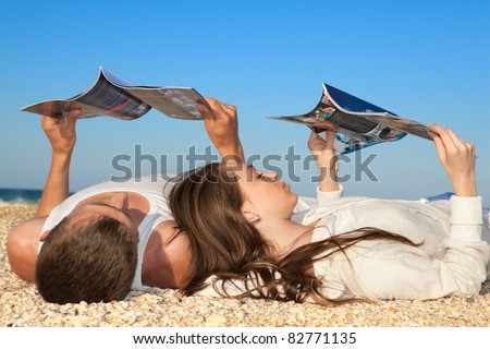 Romantic couple resting on beach and reading magazines