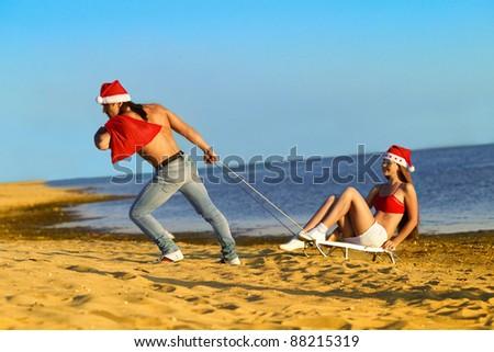 Santa pulling Sexy Santa girl on a sled at the beach.(concept: Tropical winter fun)