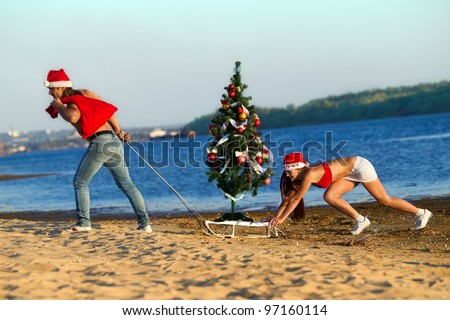 Santa pulling Christmas tree on a sled at the beach.  (concept: Tropical winter fun)