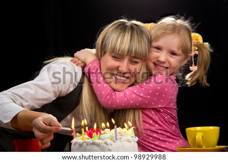 Mother burning candles in her birthday with her happy daughter