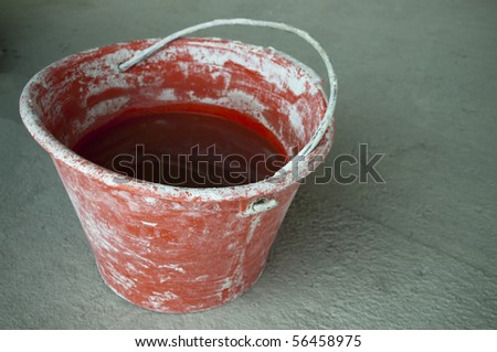 Red bricklayer bucket full of water over a gray cement floor