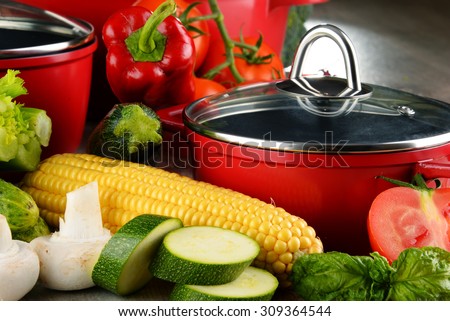 Composition with red steel pots and variety of fresh vegetables.