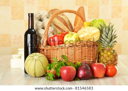 Groceries in wicker basket on kitchen table including vegetables, fruits, bakery and dairy products and wine