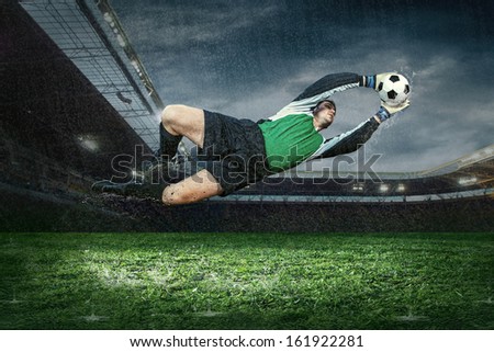 Football golkeeper with ball in action under rain in stadium