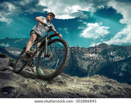 Man in helmet and glasses stay on the bicycle under sky with clouds.