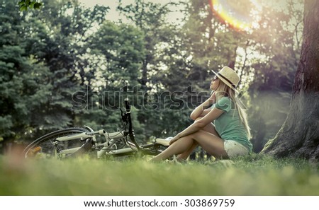 Woman sitting under sun light at day near her bicycle in the park