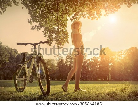Woman under sun light at day near her bicycle in the park