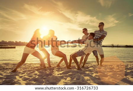 Friends funny tug of war on the beach under sunset sunlight.