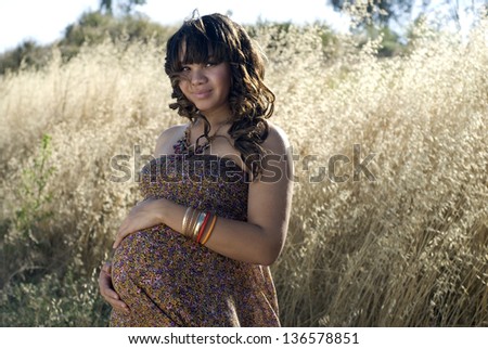 Happy pregnancy - Young mother-to-be posing in a field of tall grass.