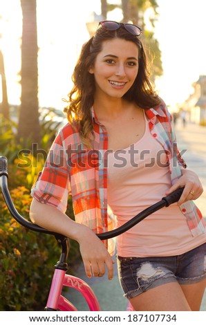 Beauty and the beach cruiser - Smiling young woman holding bike handlebars with sunglasses on her head