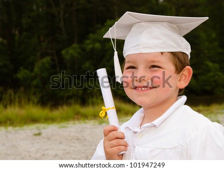 Young boy with cap and gown and certificate for preschool graduation