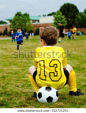 Young boy child in uniform watching organized youth soccer or football game from sidelines