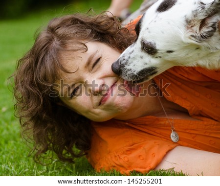 Woman making disgusted face while being licked by her pet dog