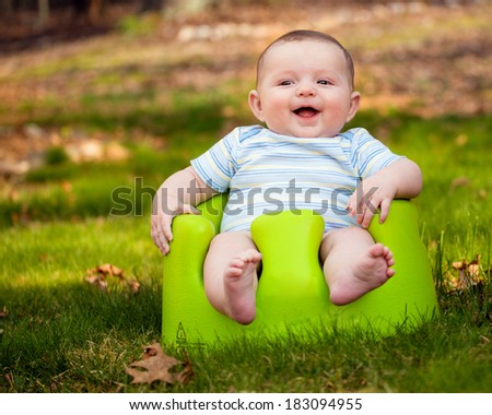 Happy infant baby boy using training Bumbo seat to sit up