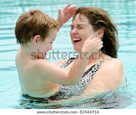 Mother and son cool off by playing in pool on hot summer day