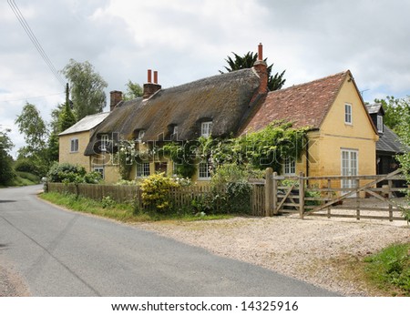 Traditional Thatched English Village Cottage on a quiet Rural Lane with a picket fence and climbing Roses.