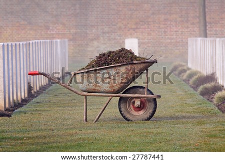 Wheelbarrow full of earth and weeds sitting on dewy grass in a War Cemetery