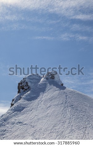 The picture shows the snow-capped peak of a mountain,  two climbers can be seen on closer inspection.