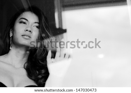 Portrait of sexy brunette woman behind the window, black and white photo