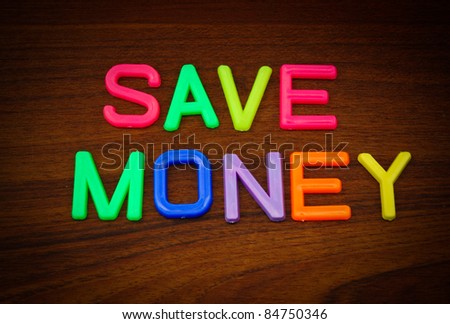 Save money in colorful toy letters on wood background