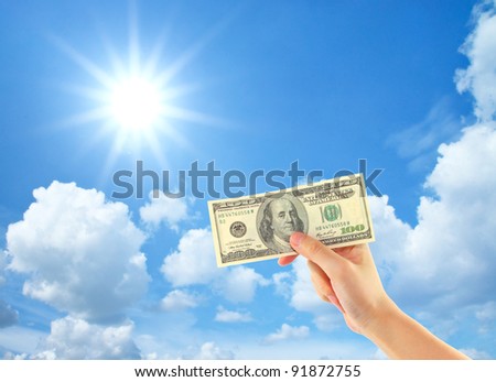 Hand showing money over sky with clouds and sun