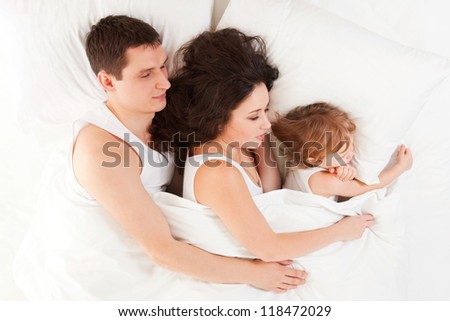 Happy family, mother, father and daughter resting on the white bed