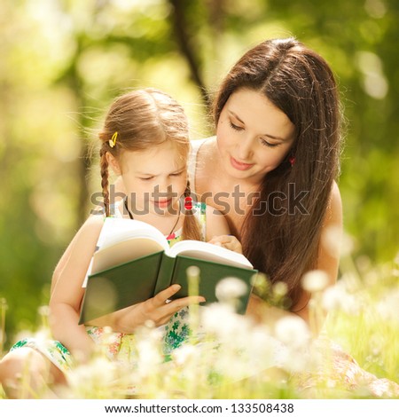 Mother with daughter read a book in the park
