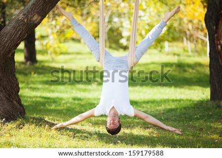 Anti-gravity Yoga, man doing yoga exercises in the park