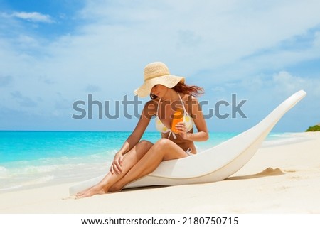 Young tanned woman in bikini sit at chaise-longue and apply sun-protection cream to her skin on the beach. Happy woman vacation. Relax on the beach. Protection of skin on the beach at summertime Stock foto © 