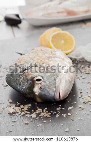 Fresh sea bream with sea salt crystals and lemon on kitchen table. Preparing seafood concept.