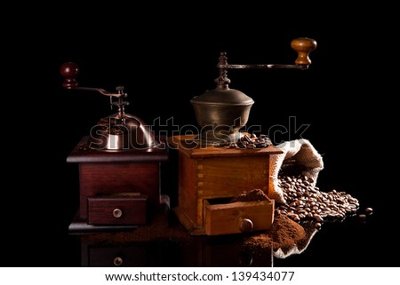 Old vintage wooden coffee mills with ground coffee, sack with coffee beans isolated on black background. Culinary aromatic coffee background.