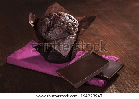 Chocolate muffin with chocolate bar on purple napkin on dark brown wooden background. Culinary delicious sweets.