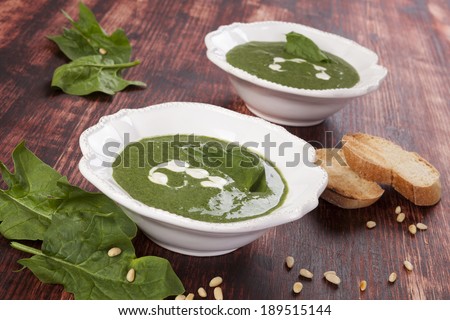 Spinach soup, fresh spinach leaves, toasted bread slices on wooden background. Culinary soup eating background.