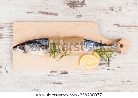 Delicious fresh mackerel fish on wooden kitchen board with lemon, rosemary and colorful peppercorns on white textured wooden background. Culinary healthy cooking.