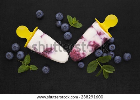 Colorful fruit ice lolly background. Two popsicle on black background with fresh berry fruit and green leaves, top view. Fresh fruit background.