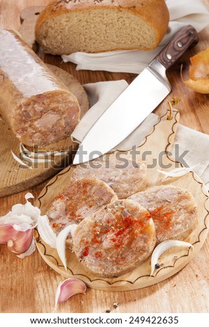 Head cheese on brown vintage cutting board with bread, garlic and onion. Traditional culinary eating.