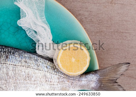 Luxurious seafood concept. Fish tail with lemon and fresh herbs on turquoise plate on background with texture, top view.