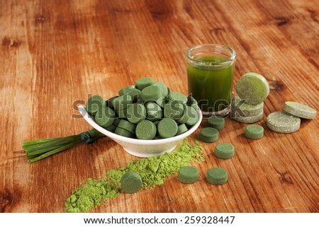 Chlorella, spirulina and wheat grass pills, ground powder on wooden background. Detox and healthy living.