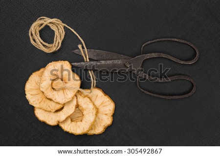 Dry apple slices on black background, with old vintage scissors and natural brown string. Healthy eating, seasonal harvest conservation.