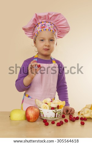 Little girl in purple cook hat and tablier making fruit salad. Healthy eating habits.