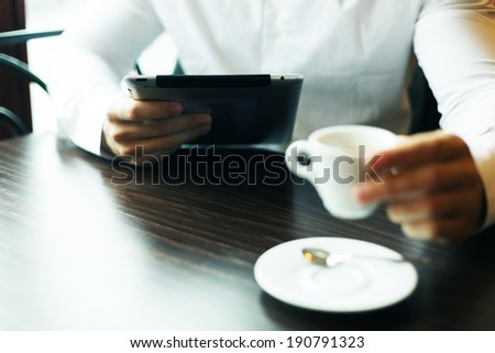 Man with tablet computer and coffee reading news at motning in cafe shop