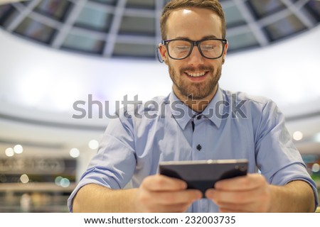 Smiling Businessman with electronic device on hand, blurred background of indoor shopping mall