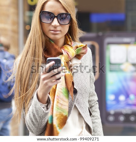 Young Woman with smartphone walking on street, downtown. In background is blured street