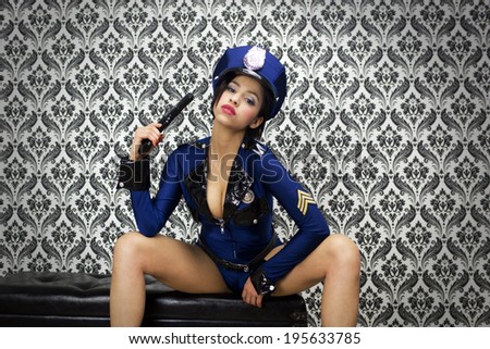 beautiful young posing dressed as a sexy police officer holding a gun against vintage wallpaper. Useful for parties, clubs and events
