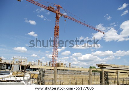 work in progress, construction site with crane in the background against the sky and clouds and lumber wood stockpile in the foreground.