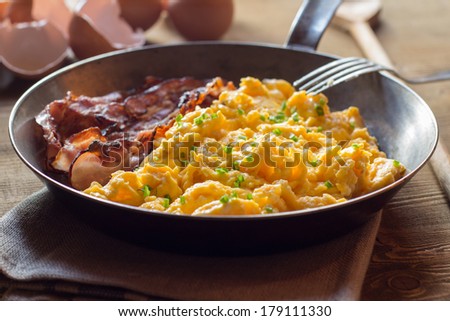 Close up of scrambled eggs with bacon in frying pan